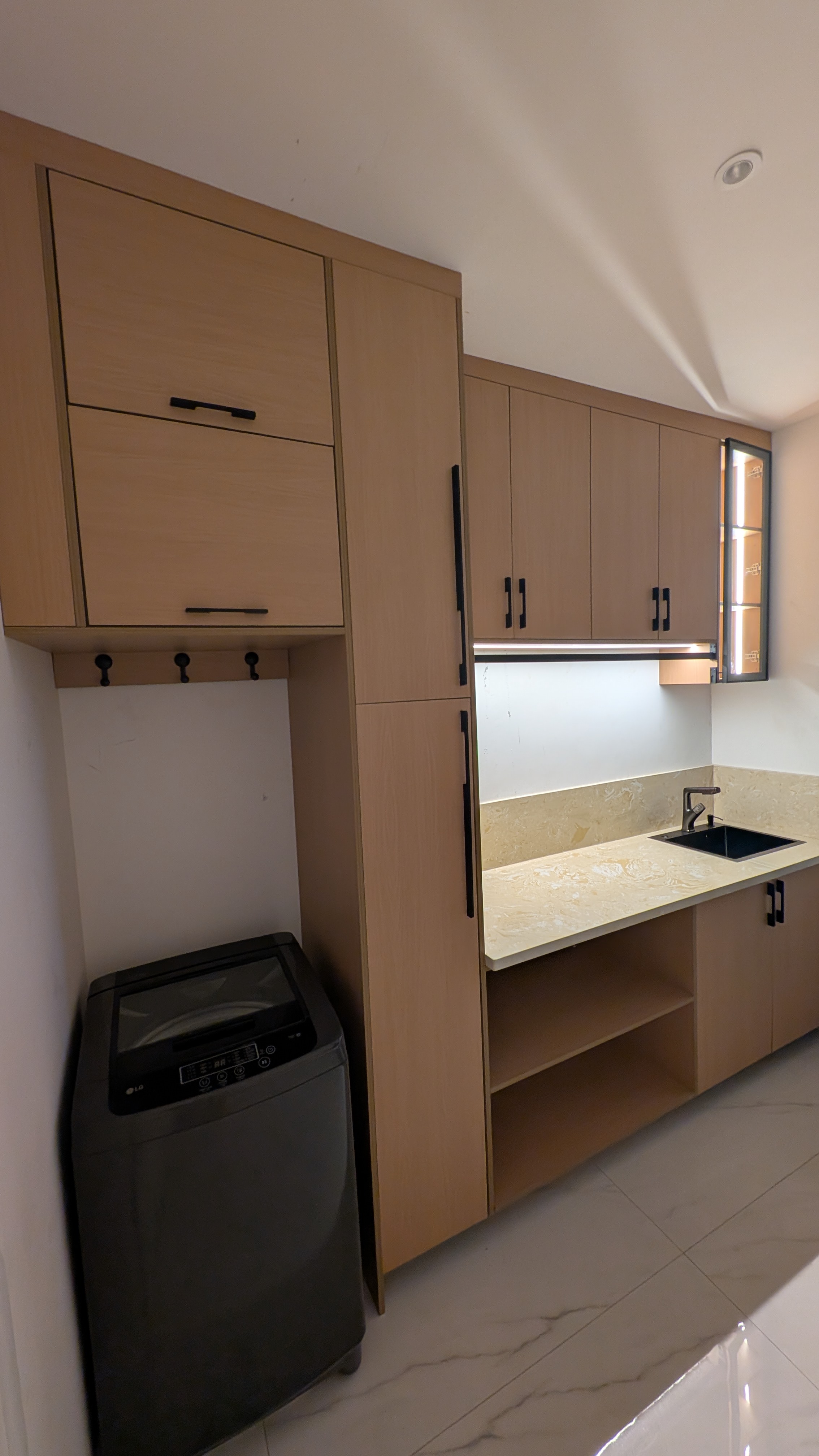 Fitted laundry room in light beech laminate with tall storage, washing machine bay, and a sink run — built by Neewoody for a private residence in Dome, Accra