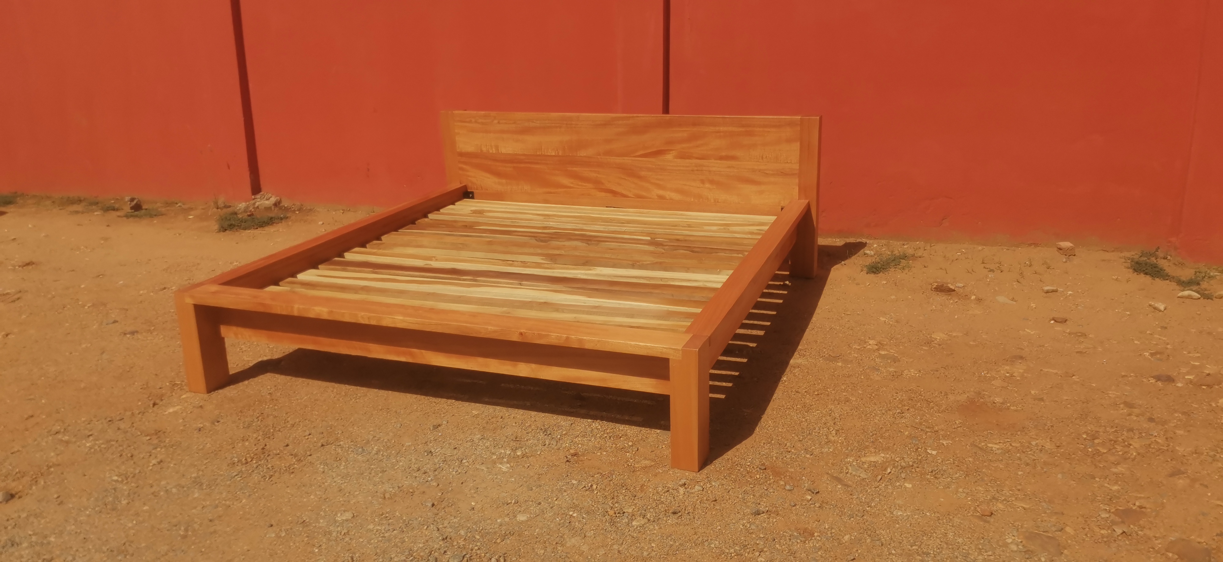 Custom platform bed in natural iroko with solid timber slab headboard, Accra
